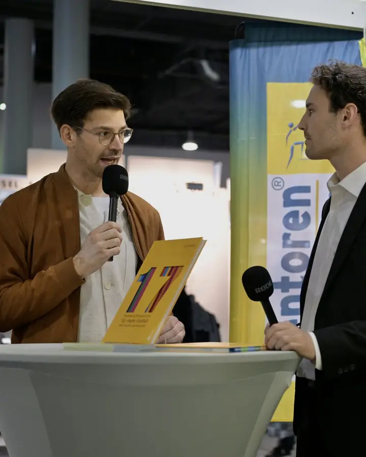 Jean Bauer spricht mit Mikrofon und dem Buch „17“ bei einem Bühnengespräch auf der Buchmesse